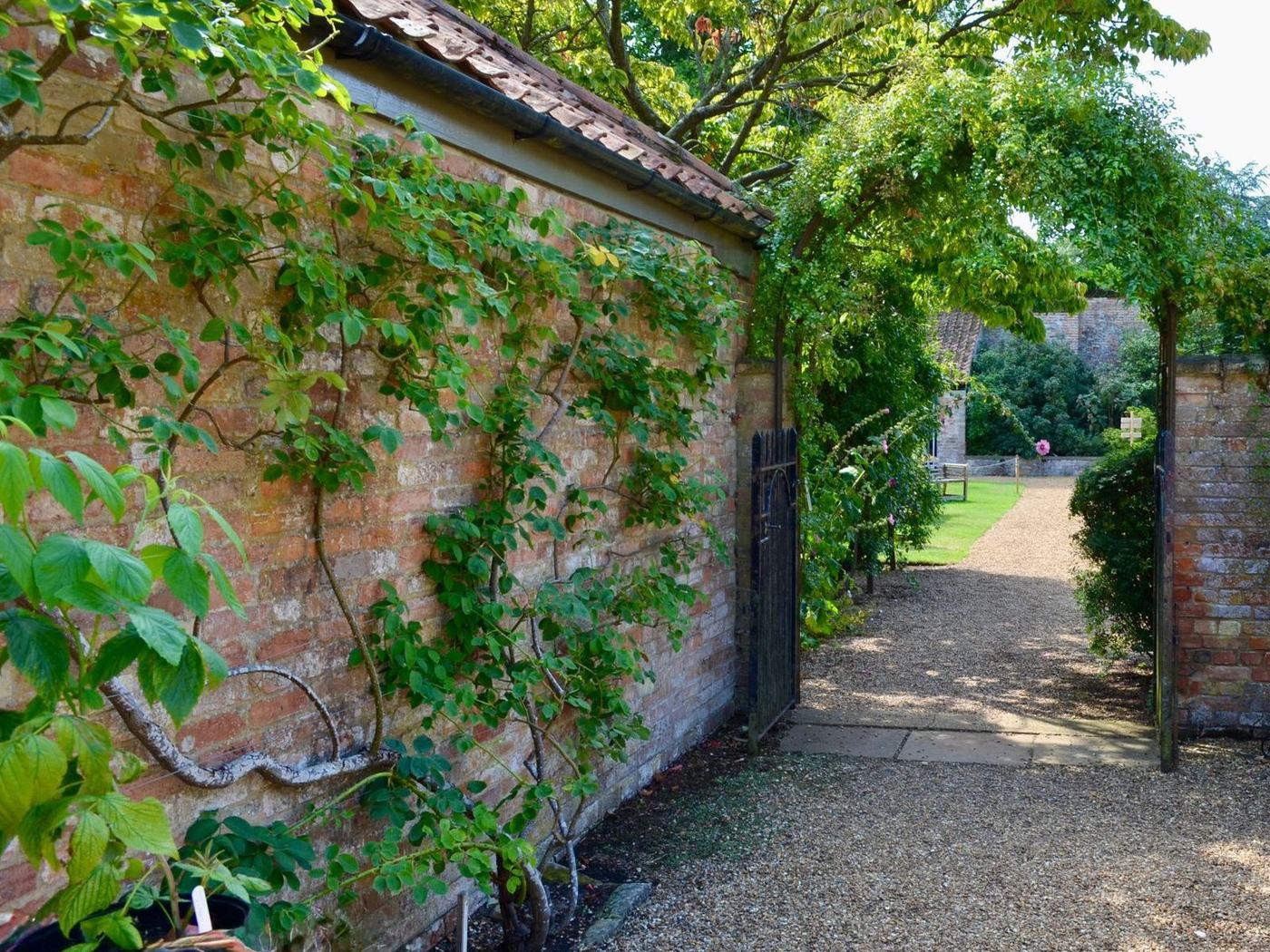 Rose-clad brick wall and gravel path leading through the gate of the restored walled garden